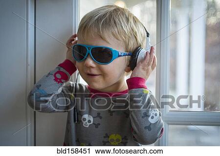 Stock Image - Caucasian boy wearing headphones and sunglasses indoors. Fotosearch
