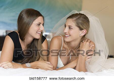 Stock Photo - Caucasian bride and bridesmaid laying on bed. Fotosearch