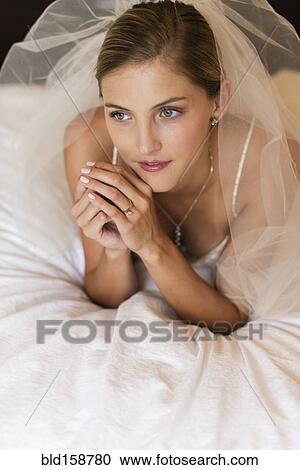 Stock Image - Caucasian bride in wedding veil laying on bed. Fotosearch