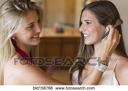 Stock Photograph - Caucasian bridesmaid applying makeup on bride. Fotosearch
