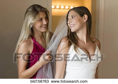 Stock Image - Caucasian bridesmaid arranging veil for bride. Fotosearch