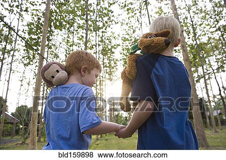 Stock Photo - Caucasian brothers carrying stuffed animals outdoors. Fotosearch