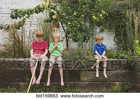 Stock Image - Caucasian brothers holding toy swords in backyard. Fotosearch