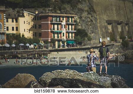 Stock Photo - Caucasian brothers photographing beach from rock formations, Cinque Terre, Liguria, Italy. Fotosearch