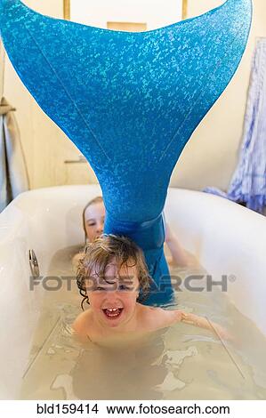 Picture - Caucasian children playing with mermaid tail in bath. Fotosearch