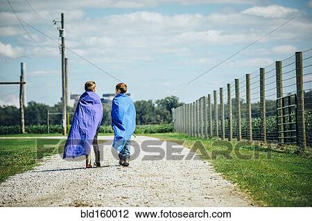 Stock Image - Caucasian children wearing capes on dirt road. Fotosearch