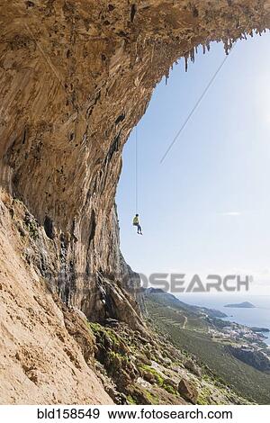 Stock Photo - Caucasian climber hanging from cable on rock wall. Fotosearch