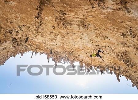 Stock Image - Caucasian climber scaling rock wall. Fotosearch