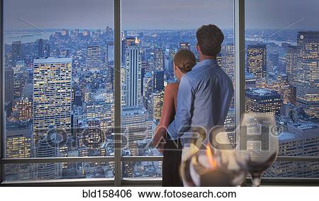 Stock Photograph - Caucasian couple admiring New York cityscape from window, New York, United States. Fotosearch