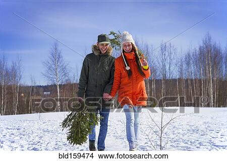 Picture - Caucasian couple carrying tree branch in snowy field. Fotosearch