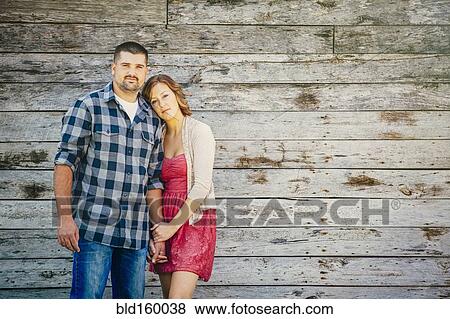 Stock Photo - Caucasian couple holding hands near wooden building. Fotosearch