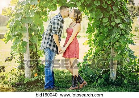 Stock Image - Caucasian couple kissing under leafy arch. Fotosearch