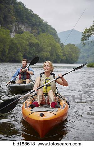 Stock Photo - Caucasian couple paddling kayaks in remote river. Fotosearch