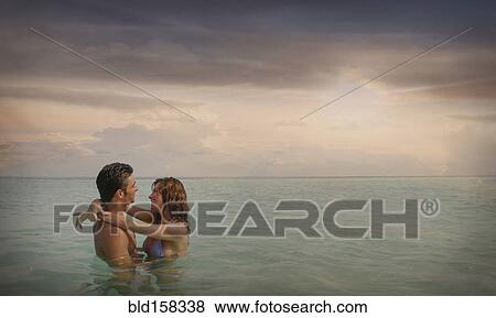 Stock Photo - Caucasian couple swimming and hugging in ocean. Fotosearch