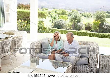 Stock Photography - Caucasian couple using cell phone and digital tablet on sofa. Fotosearch