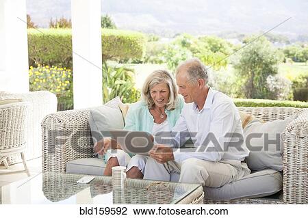 Stock Image - Caucasian couple using digital tablet on sofa outdoors. Fotosearch