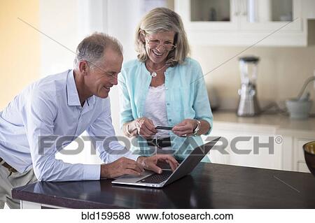 Caucasian couple using laptop on kitchen counter View Large Photo Image Stock Photo - Caucasian couple using laptop on kitchen counter. Fotosearch