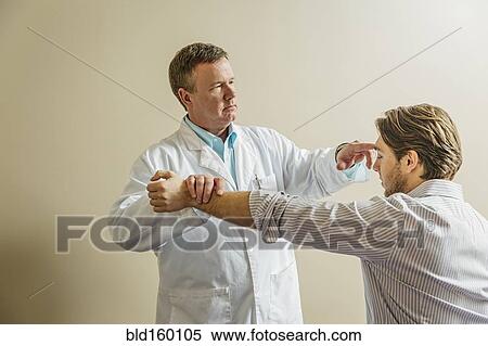 Stock Photography - Caucasian doctor adjusting arm of patient. Fotosearch