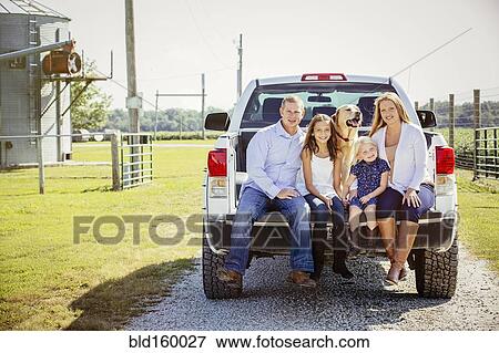 Stock Photo - Caucasian family and dog sitting in truck bed on farm. Fotosearch