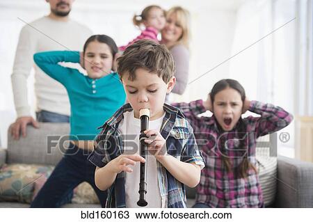 Stock Image - Caucasian family covering ears with boy playing recorder. Fotosearch