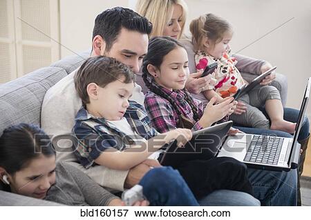 Stock Photo - Caucasian family using technology on sofa. Fotosearch