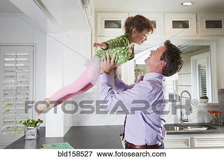 Stock Photo - Caucasian father and daughter playing in kitchen. Fotosearch