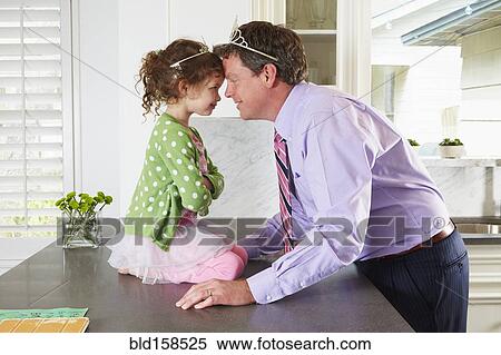 Stock Photography - Caucasian father and daughter wearing tiaras in kitchen. Fotosearch