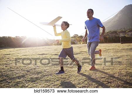 Stock Image - Caucasian father and son flying model airplane in field. Fotosearch