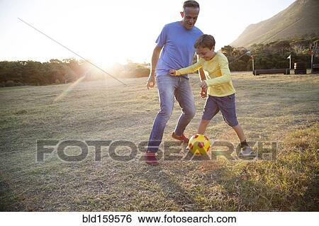 Stock Photograph - Caucasian father and son playing soccer in field. Fotosearch