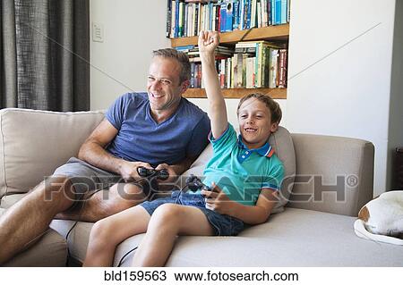 Caucasian father and son playing video games on sofa View Large Photo Image Stock Image - Caucasian father and son playing video games on sofa. Fotosearch