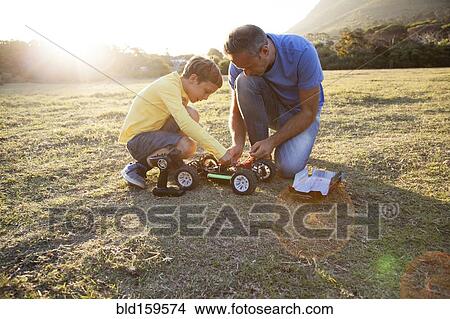 Picture - Caucasian father and son playing with remote control cars in field. Fotosearch