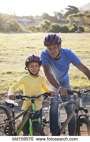 Stock Image - Caucasian father and son riding bicycles on dirt path. Fotosearch