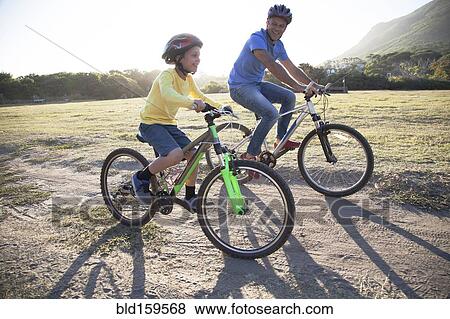 Stock Photo - Caucasian father and son riding bicycles on dirt path. Fotosearch