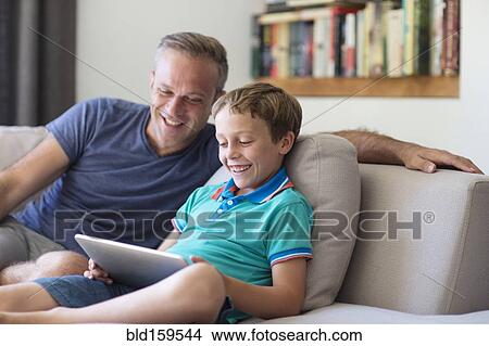 Picture - Caucasian father and son using digital tablet on sofa. Fotosearch
