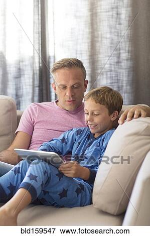 Stock Photo - Caucasian father and son using digital tablet on sofa. Fotosearch