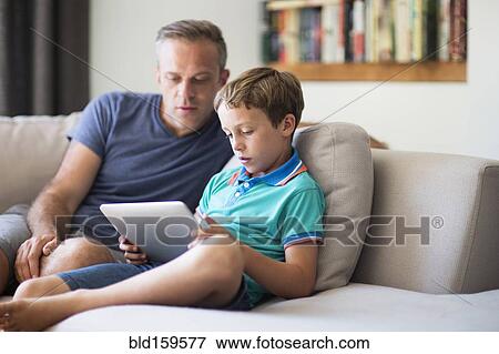 Stock Photo - Caucasian father and son using digital tablet on sofa. Fotosearch