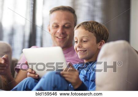 Stock Photograph - Caucasian father and son using digital tablet on sofa. Fotosearch