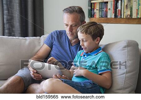 Stock Photography - Caucasian father and son using digital tablet on sofa. Fotosearch