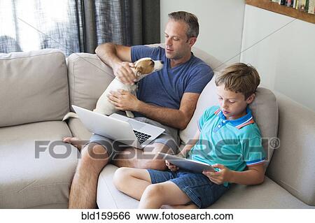 Stock Photograph - Caucasian father and son using technology on sofa. Fotosearch