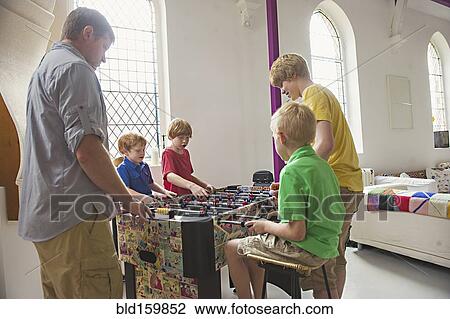 Stock Image - Caucasian father and sons playing foosball. Fotosearch