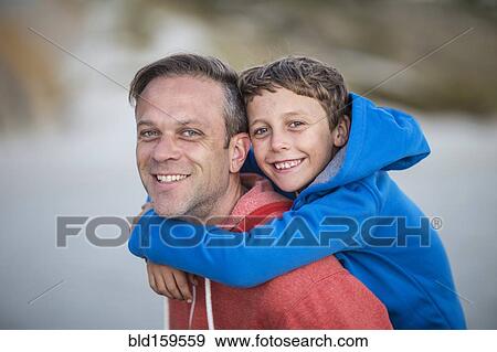 Stock Photo - Caucasian father carrying son piggyback outdoors. Fotosearch
