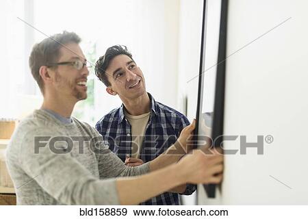Caucasian gay couple hanging picture on wall View Large Photo Image Stock Photo - Caucasian gay couple hanging picture on wall. Fotosearch