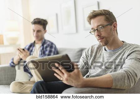 Picture - Caucasian gay couple relaxing on sofa. Fotosearch