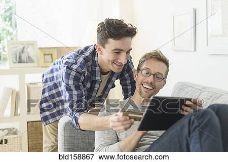 Stock Photo - Caucasian gay couple shopping online on digital tablet. Fotosearch