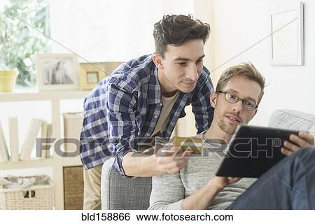Caucasian gay couple shopping online on digital tablet View Large Photo Image Stock Photograph - Caucasian gay couple shopping online on digital tablet. Fotosearch