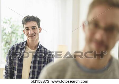 Stock Image - Caucasian gay couple smiling in home. Fotosearch