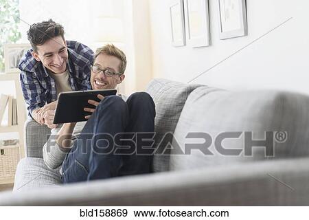 Stock Photo - Caucasian gay couple using digital tablet on sofa. Fotosearch