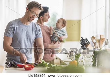 Picture - Caucasian gay fathers and baby cooking in kitchen. Fotosearch