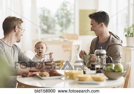 Stock Image - Caucasian gay fathers and baby eating breakfast. Fotosearch