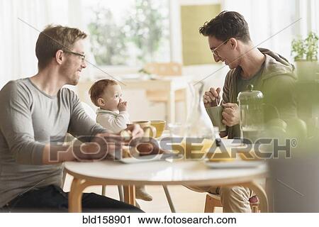 Stock Image - Caucasian gay fathers and baby eating breakfast. Fotosearch
